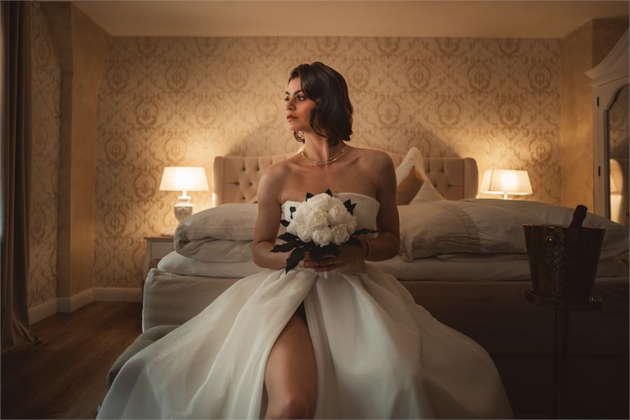 Braut mit weißem Rosenstrauß in einer warm beleuchteten Hotelsuite